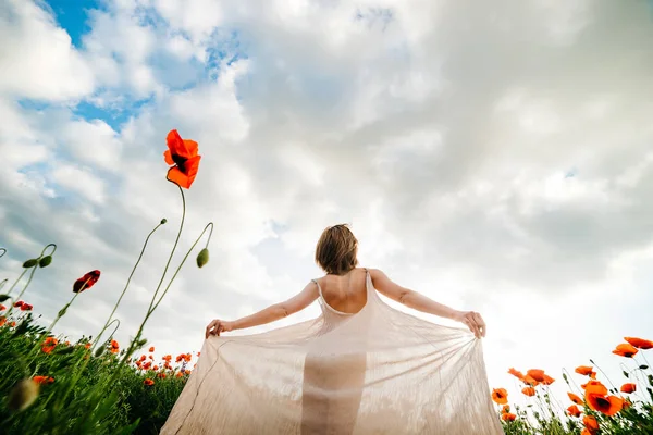 Young woman in a long white dress in a poppy field against a blue sky — Stock Photo, Image