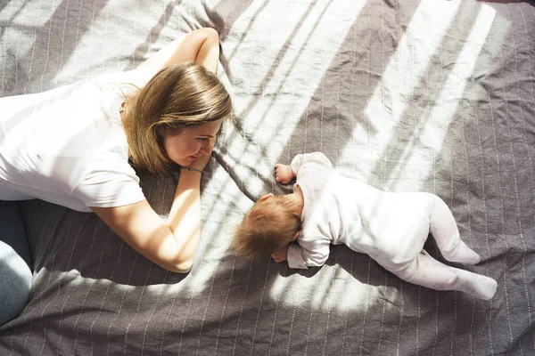 Madre con su hijo recién nacido yacía en la cama bajo los rayos del sol —  Fotos de Stock