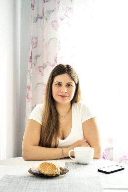 Beyaz tişörtlü genç, uzun saçlı sarışın bir kadın çay içiyor. 