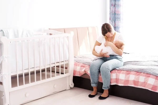 Madre con un bebé recién nacido en brazos sentada en la habitación de los niños en la cama —  Fotos de Stock