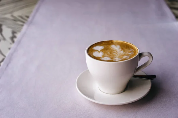 White mug on a saucer with cappuccino and beautiful heart-shaped milk foam