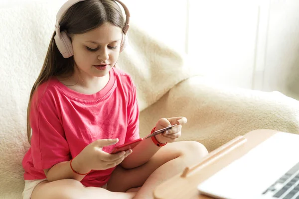 Chica alegre en auriculares rosados se sienta con un teléfono en la mano y una tarjeta de crédito —  Fotos de Stock
