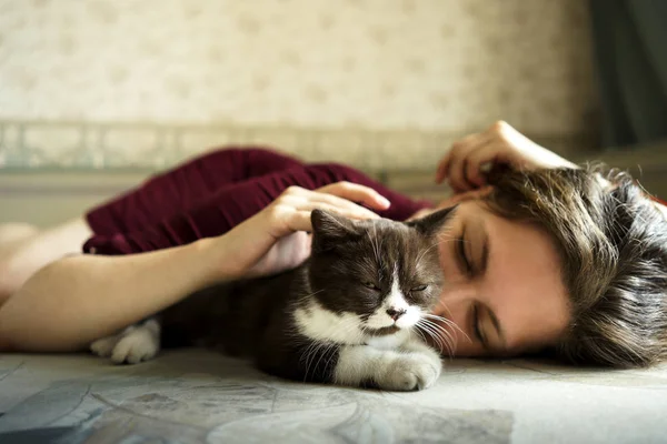 Una mujer y un pequeño gatito británico blanco y negro yacen en el sofá . —  Fotos de Stock