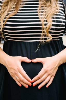 Uzun sarı saçlı siyah beyaz çizgili elbiseli hamile bir kadın 