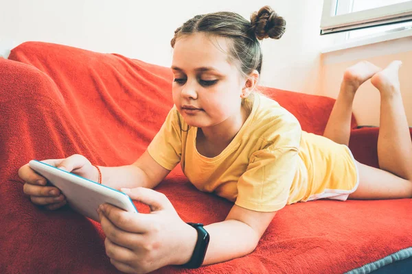Una chica está acostada en un sofá rojo en el balcón con una tableta —  Fotos de Stock