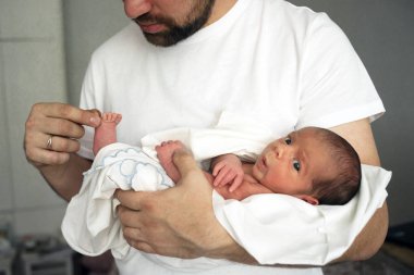Baba beyaz bir bez elinde çıplak yeni doğan oğlu tutar