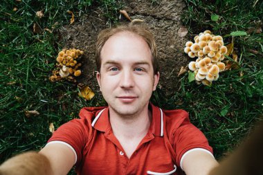 Kırmızı gömlekli aptal bir adam mantarların arasında yerde yatıyor.