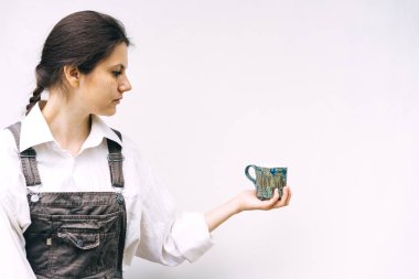 Elinde beyaz bir duvarın arka planında mavi seramik kupa olan kadın