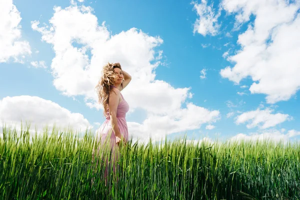 Long-haired woman in a pink dress on a field of green wheat and wild — Stock Photo, Image