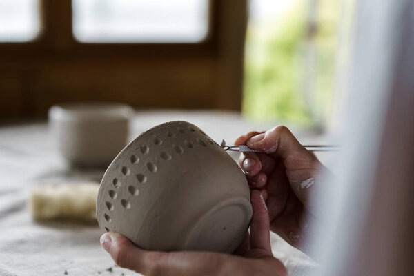 Female hands handle the edge of a wet clay bowl with a stick