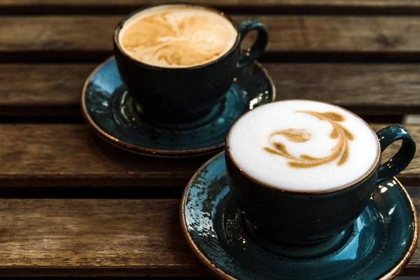 Ahşap masada latte sanatı ile kapuçino iki güzel bardak.