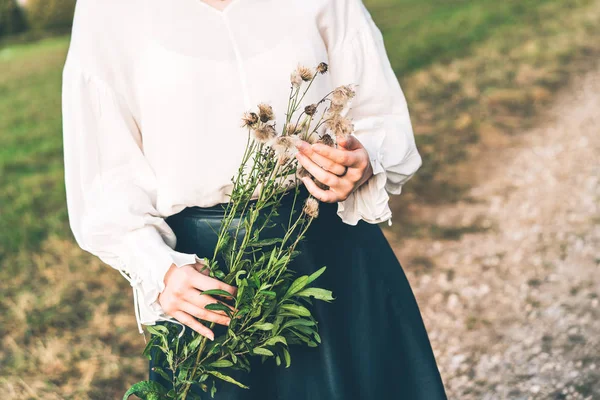 Young woman in a field holds a branch of fluffy autumn dandelions in her hands — Stock Photo, Image