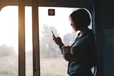 Elinde telefon ve bir fincan kahve olan güzel bir kadın kapıdaki banliyö treninin arabasında duruyor. Turist seyahat konsepti. Sınırlar olmadan iletişim