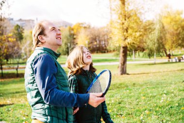 Okul çağındaki bir baba ve oğlu badminton raketiyle konuşuyor.