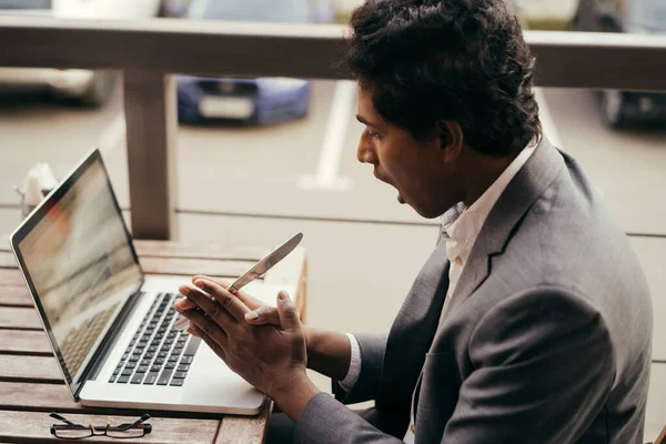 Young handsome Indian man in a summer cafe with a laptop with a table knife