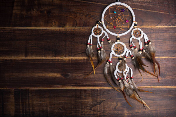Dream catcher with feathers threads and beads rope hanging spiritual folk american native indian amulet isolated on brown wooden textured background.Concept prevent evil in Halloween
