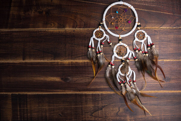 Dream catcher with feathers threads and beads rope hanging spiritual folk american native indian amulet isolated on brown wooden textured background.Concept prevent evil in Halloween