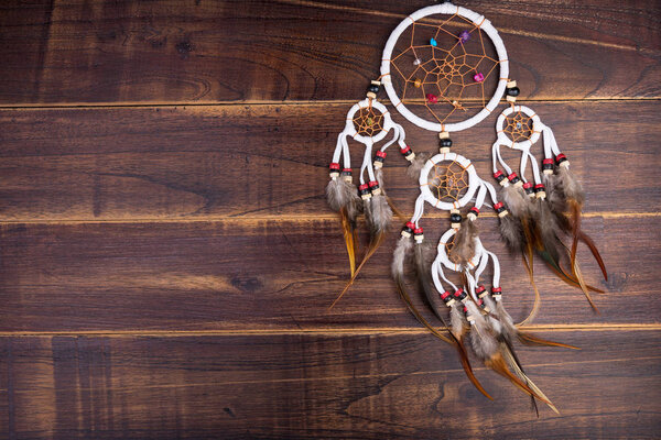 Dream catcher with feathers threads and beads rope hanging spiritual folk american native indian amulet isolated on brown wooden textured background.Concept prevent evil in Halloween
