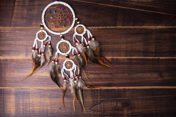 Dream catcher with feathers threads and beads rope hanging spiritual folk american native indian amulet isolated on brown wooden textured background.Concept prevent evil in Halloween