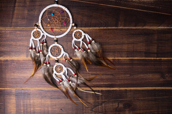 Dream catcher with feathers threads and beads rope hanging spiritual folk american native indian amulet isolated on brown wooden textured background.Concept prevent evil in Halloween