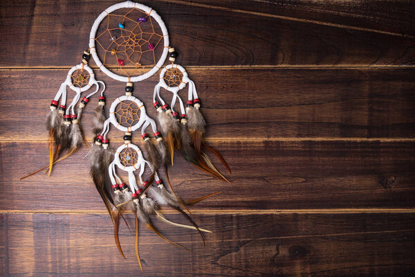 Dream catcher with feathers threads and beads rope hanging spiritual folk american native indian amulet isolated on brown wooden textured background.Concept prevent evil in Halloween