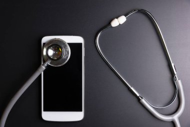 Mobil bir akıllı telefon, siyah arka plan üzerinde izole kompozisyon yüzey üzerinde sağlık stetoskop aracı. Sağlık Güvenlik kavramı kontrol.