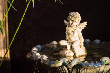 Yaşlı beyaz melek Cupid heykel oturan su çeşmesi.