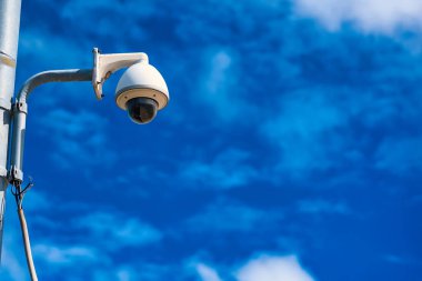 Mavi gökyüzü arka planında bir direkteki güvenlik kamerası.