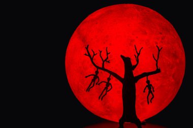 Kemiklerine kadar asılmış bir adamla ölü bir ağacın silueti. Arka planda kırmızı bir dolunay var. Cadılar Bayramı korku konsepti.