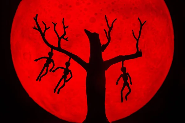 男と死んで立っている木のシルエットは 骨に死者を絞首刑にした 背景に赤い満月があります ハロウィンホラーのコンセプト — ストック写真