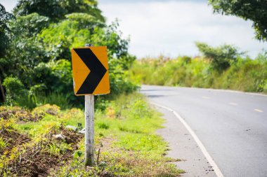 Çimlerin üzerinde sağa dönüş işareti olan yemyeşil kırsal bölgede yol kıvrımlı.