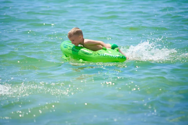 男孩骑着玩具在海里游泳充气鳄鱼 — 图库照片