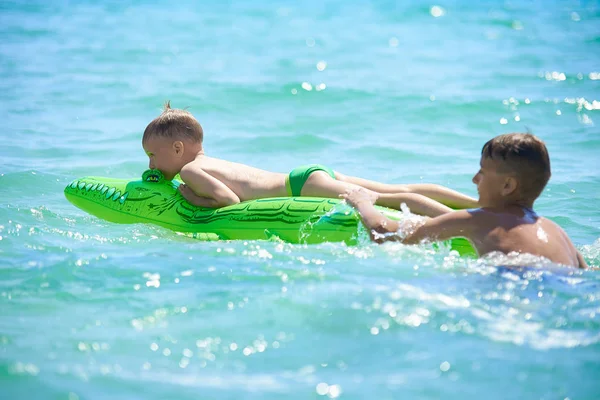 哥哥十几岁的弟弟滚到海里的玩具充气鳄鱼 — 图库照片