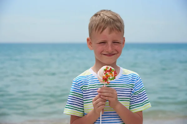 Rapaz pequeno que come na praia doce doces — Fotografia de Stock