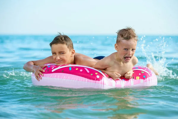 DOS NIÑOS AHORRA EN UN CÍRCULO INFLATABLE EN EL MAR — Foto de Stock