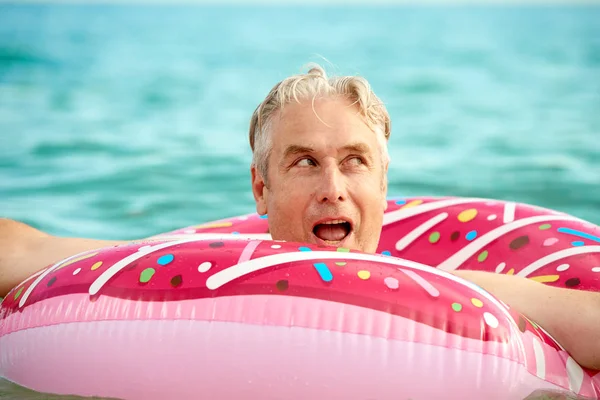 Gris de pelo divertido hombre nada en un círculo inflable en el mar — Foto de Stock