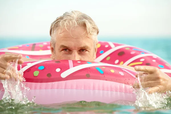 Homem engraçado de cabelos grisalhos nada em um círculo inflável no mar — Fotografia de Stock