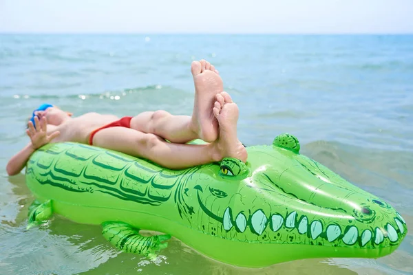 NIÑO NADA EN EL MAR SOBRE EL JUGUETE CROCODÍLICO INFLATABLE . — Foto de Stock