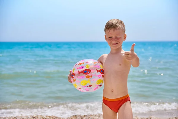 Menino 7 anos com bola inflável na praia perto do mar — Fotografia de Stock