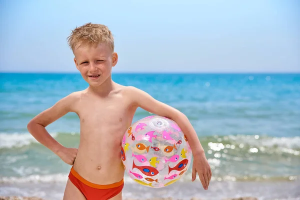 Menino 7 anos com bola inflável na praia perto do mar — Fotografia de Stock