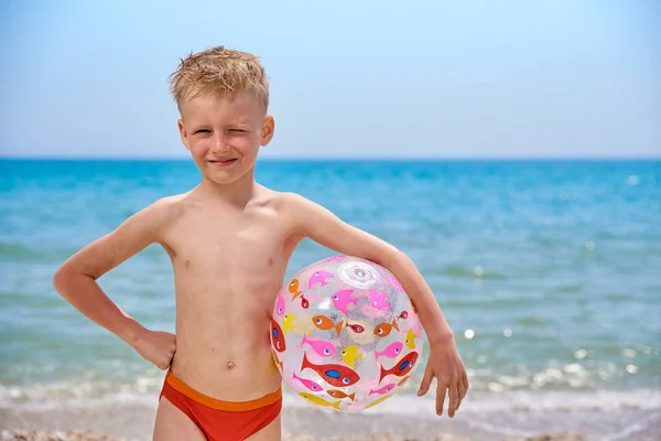 Menino 7 anos com bola inflável na praia perto do mar — Fotografia de Stock