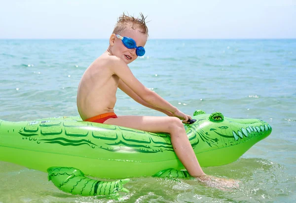 NIÑO NADA EN EL MAR SOBRE EL JUGUETE CROCODÍLICO INFLATABLE . — Foto de Stock