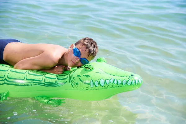 Menino dos adolescentes na água os óculos de proteção nadam no crocodilo inflável do brinquedo. — Fotografia de Stock