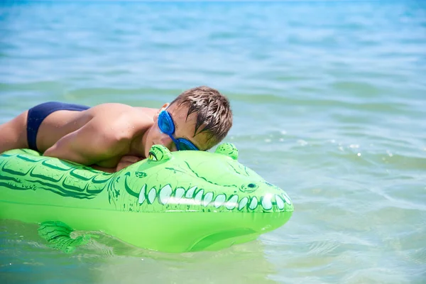 Menino dos adolescentes na água os óculos de proteção nadam no crocodilo inflável do brinquedo. — Fotografia de Stock