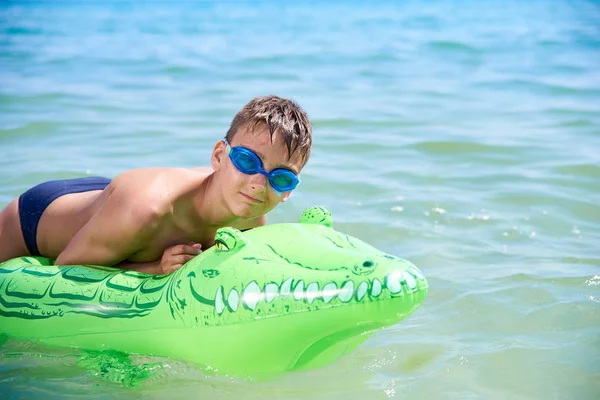 Menino dos adolescentes na água os óculos de proteção nadam no crocodilo inflável do brinquedo. — Fotografia de Stock