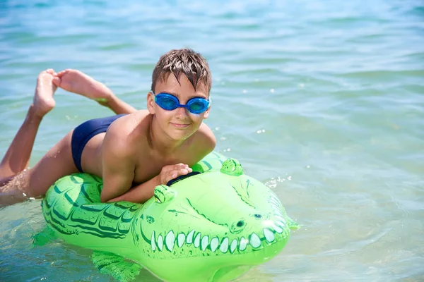 Menino dos adolescentes na água os óculos de proteção nadam no crocodilo inflável do brinquedo. — Fotografia de Stock