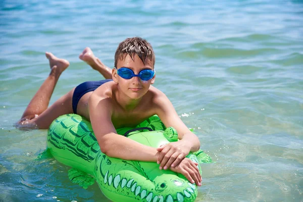 Menino dos adolescentes na água os óculos de proteção nadam no crocodilo inflável do brinquedo. — Fotografia de Stock