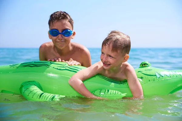 BOY OF TEENAGERS IN WATER GOGGLES SWIMS ON THE INFLATABLE TOY CROCODILE. — Stock Photo, Image