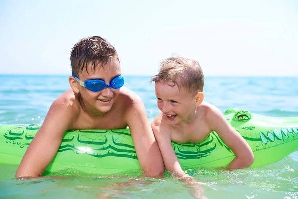 BOY OF TEENAGERS IN WATER GOGGLES SWIMS ON THE INFLATABLE TOY CROCODILE. — Stock Photo, Image