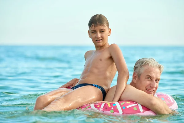 Abuelo y nieto nadan en el mar en un círculo inflable — Foto de Stock